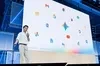 一位身穿白色襯衫的男生於台上分享的畫面，背景充滿各種 Google 旗下產品的 logo的
